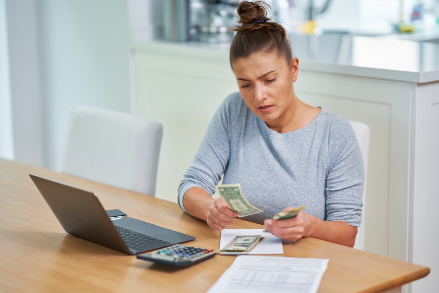 A woman counting dollars and working out her monthly outgoings to avoid defaulting on a personal loan, to represent ‘What Happens If I Default on a Personal Loan?’.