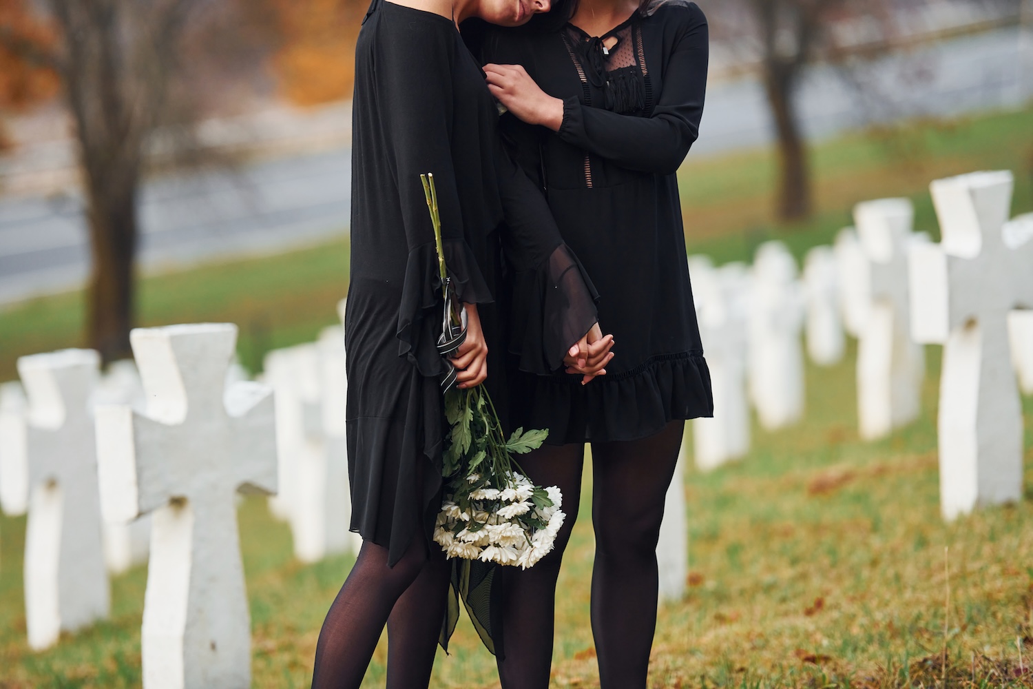 Two young women in black clothes visiting cemetery with many white crosses.