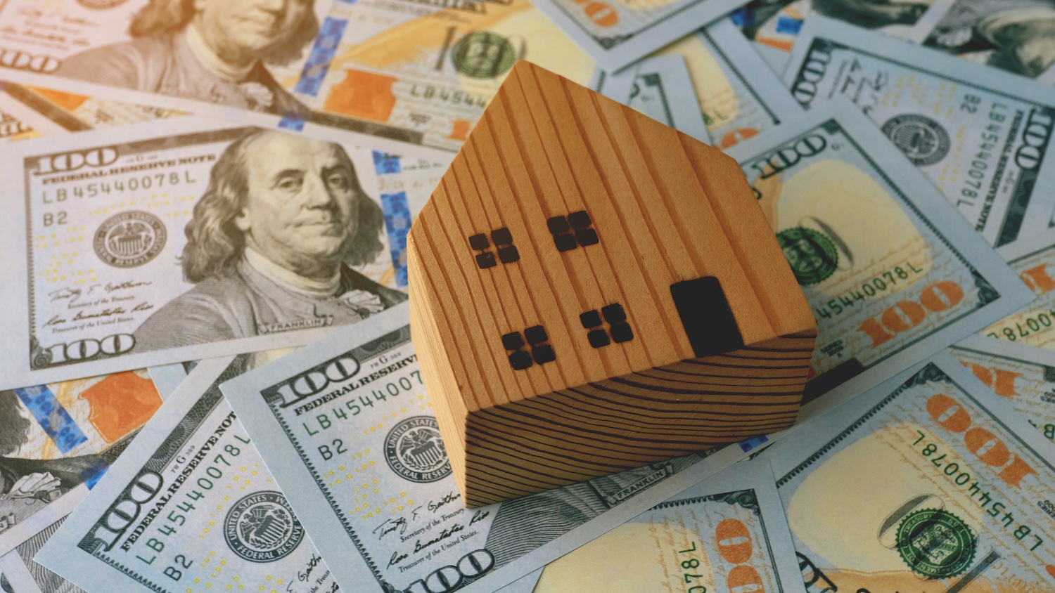 A wooden toy house on top of dollars to show personal loans vs home equity loans